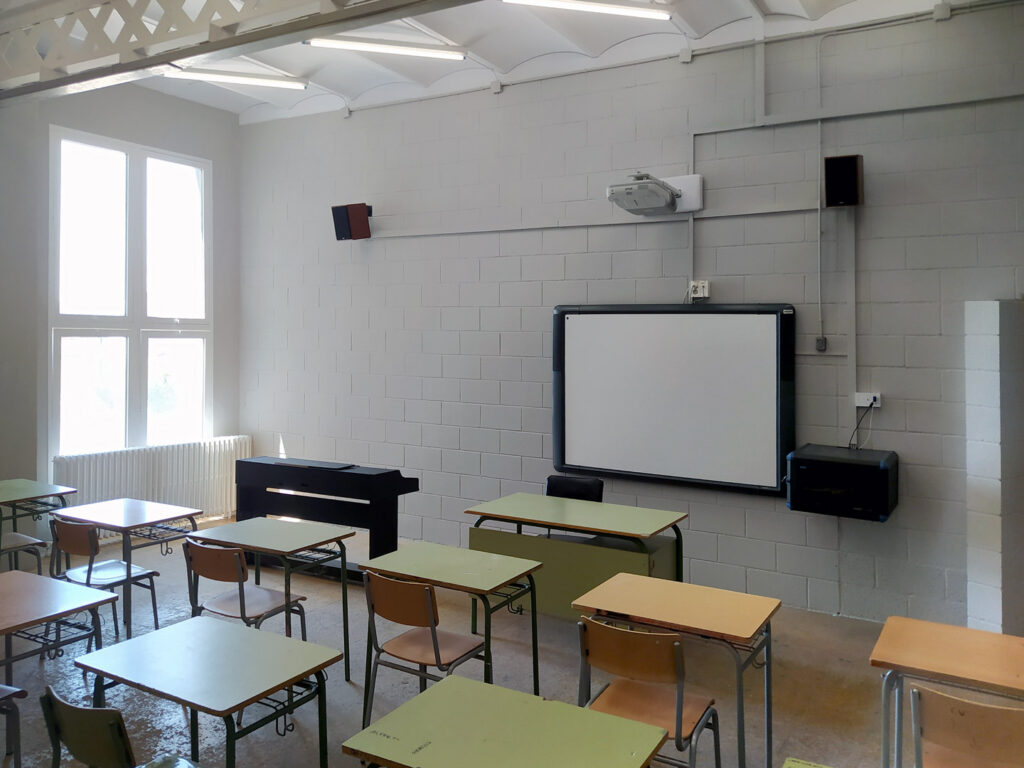 Una aula amb escriptoris organitzats i una pantalla de projector al capdavant, acabada de pintar.